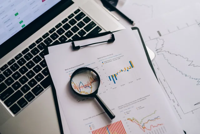 Overhead view of financial charts, laptop, and magnifying glass, ideal for business analysis themes. Comparer les indicateurs avancés du KOF et du SECO