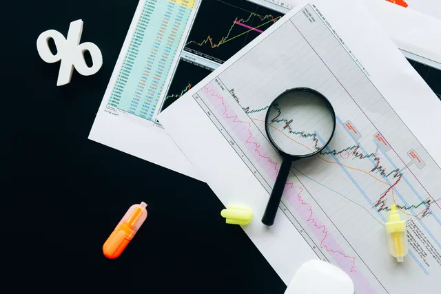 High-angle view of financial charts, showcasing stock market analysis with magnifying glass and highlighters. Suivre l'inflation suisse à partir de l'indice des prix à la consommation